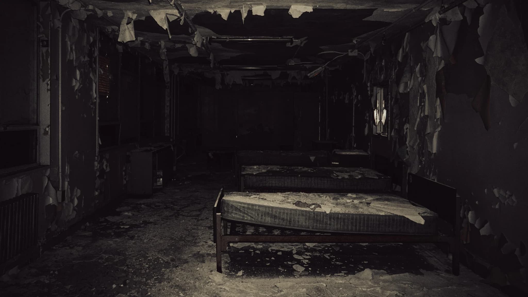 Dark abandoned ward with peeling paint and old bed frames