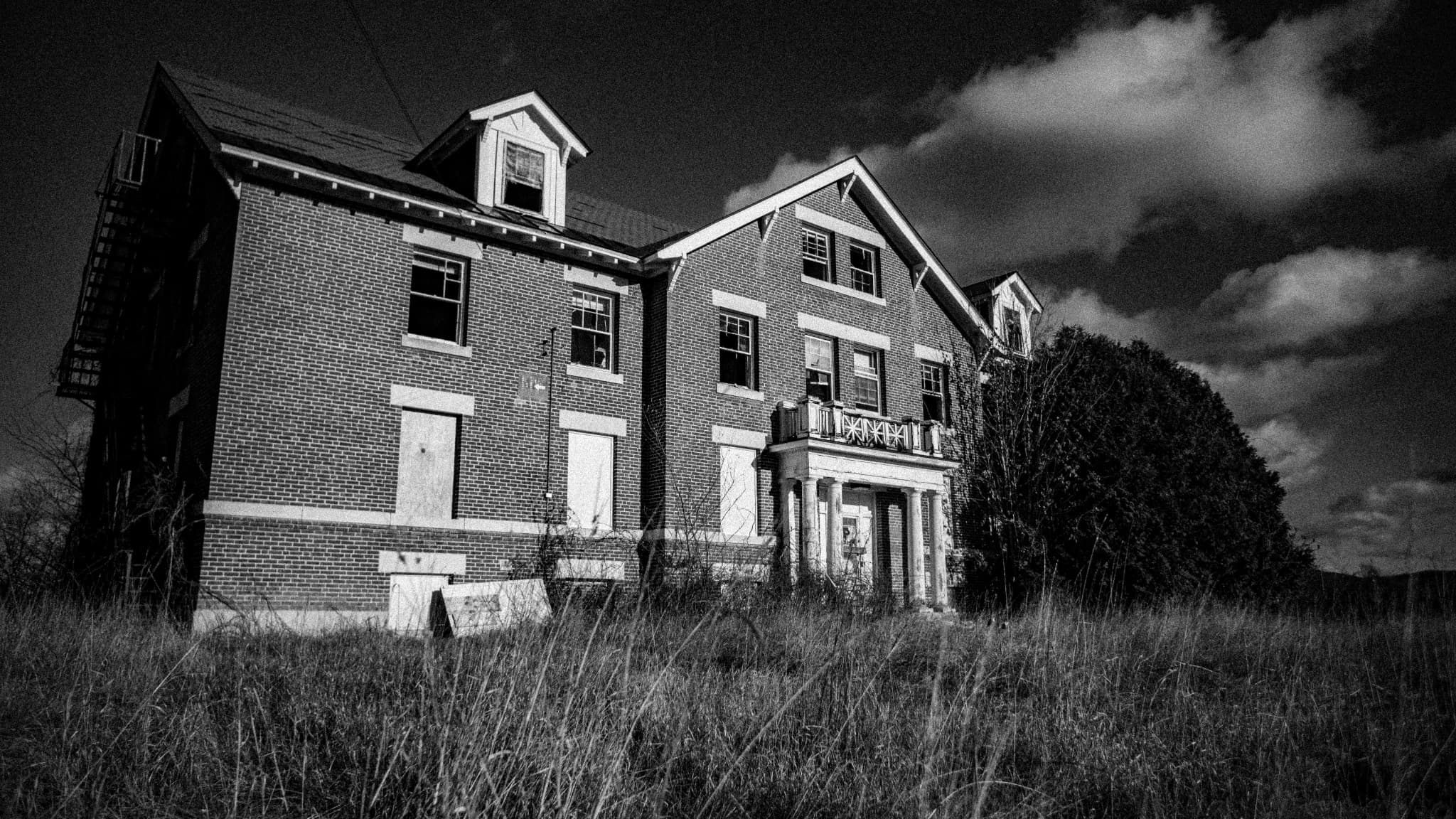 Black and white abandoned brick house beneath dramatic clouds
