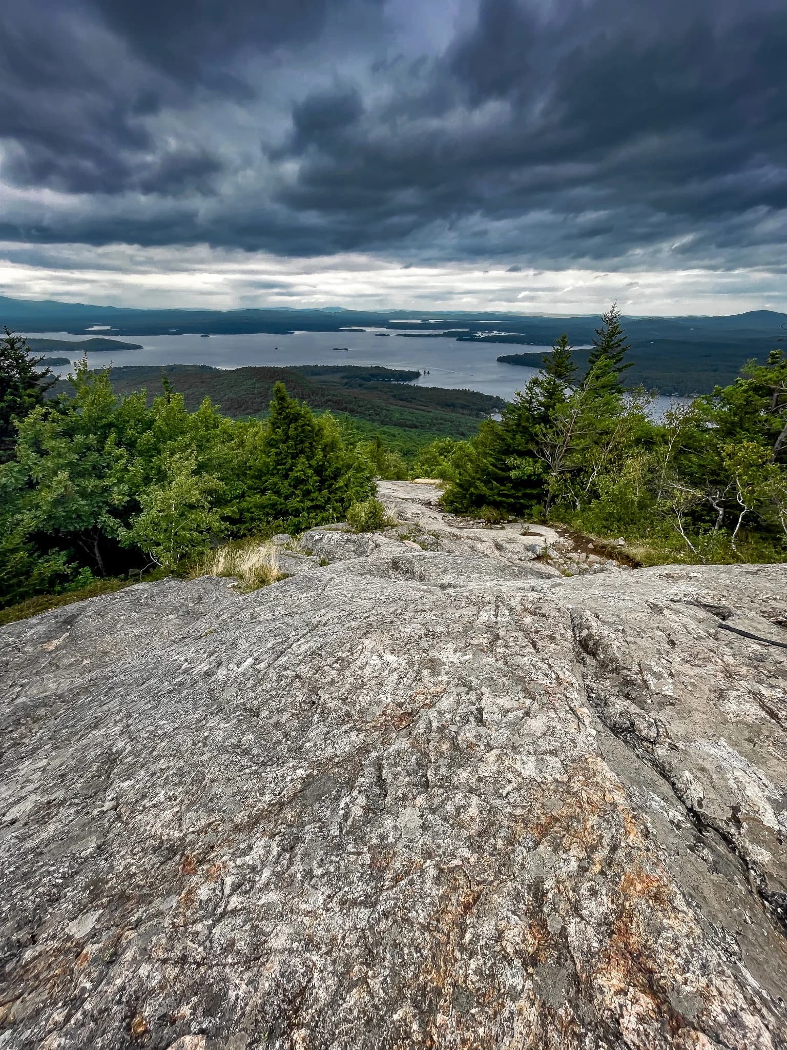 Expansive lake beneath layered dark storm clouds from a rocky summit